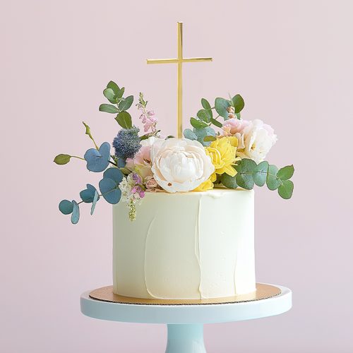 Gold fine cross cake topper by Cake & Candle displayed on a decorated celebration cake