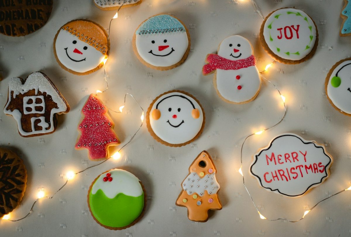 Decorated Christmas cookies including snowmen, trees and a gingerbread house beside fairy lights