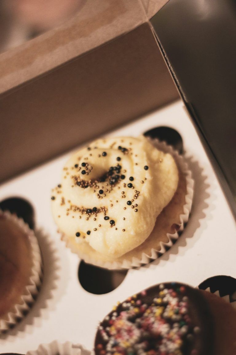 Cupcakes with pale frosting and sprinkles in a cardboard cupcake box